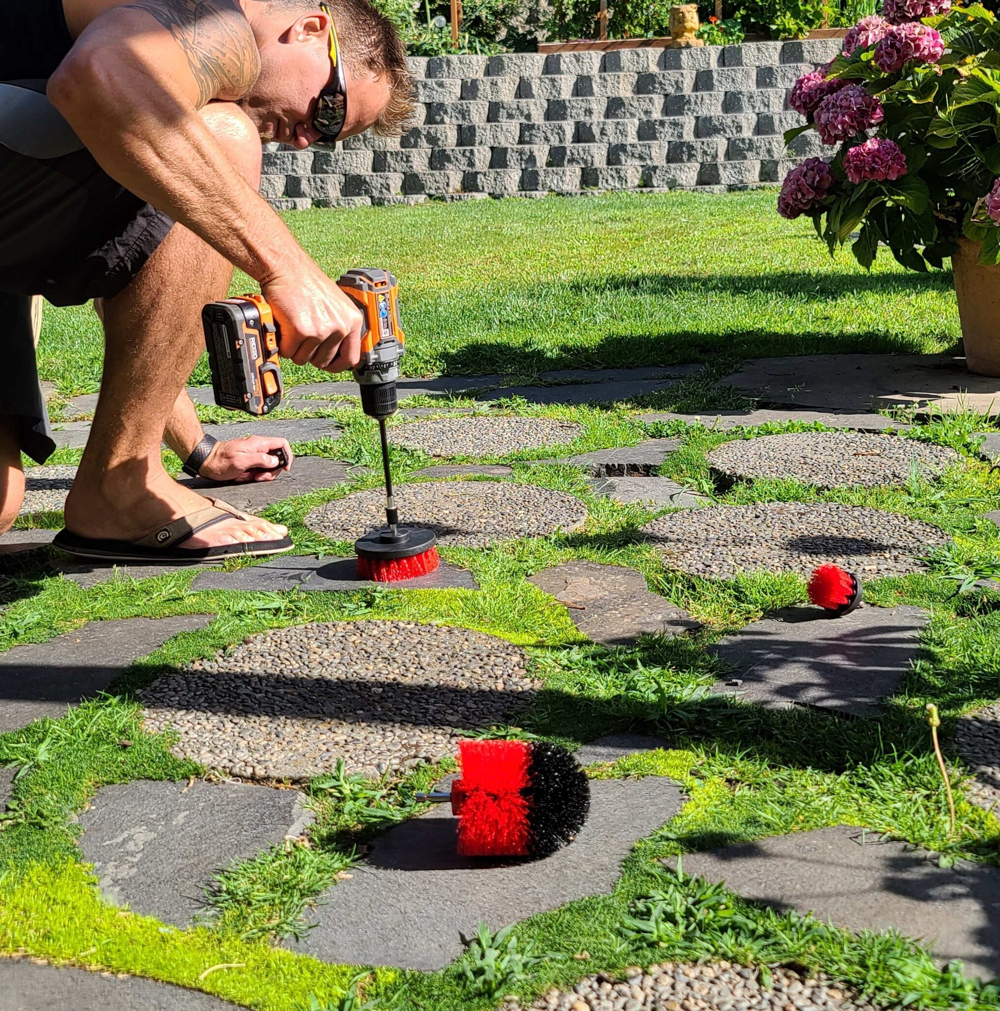 Man using drill brush from Drill Brush 3 Pack to clean outdoor stone pathway with medium stiffness bristles