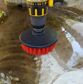 Red flat 5 inch cleaning drill brush with stiff nylon bristles attached to drill for heavy-duty scrubbing on outdoor surface.