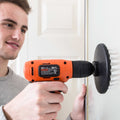 Man using orange drill with white soft bristle brush attachment to clean wall surface