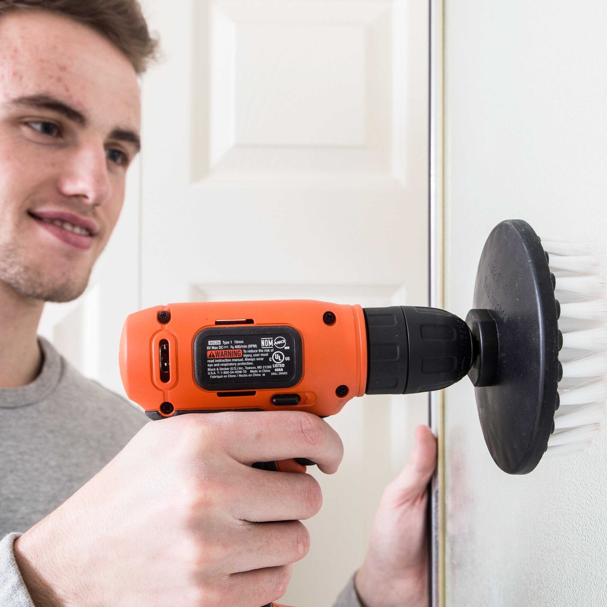 Man using orange drill with white soft bristle brush attachment to clean wall surface